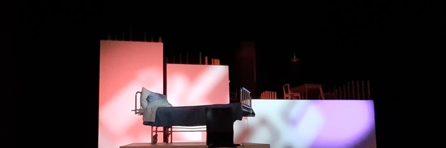 Sairaalavuode ja kaksi valaistua seinää mustassa tilassa.