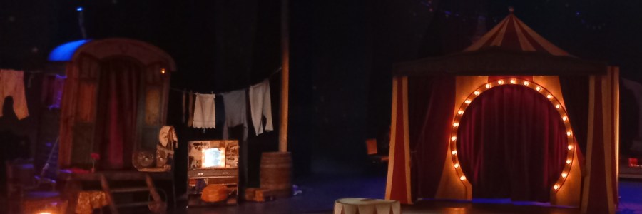 Näyttämökuva, jossa näkyy sirkusvaunu ja sirkuksen areena ja teltta.