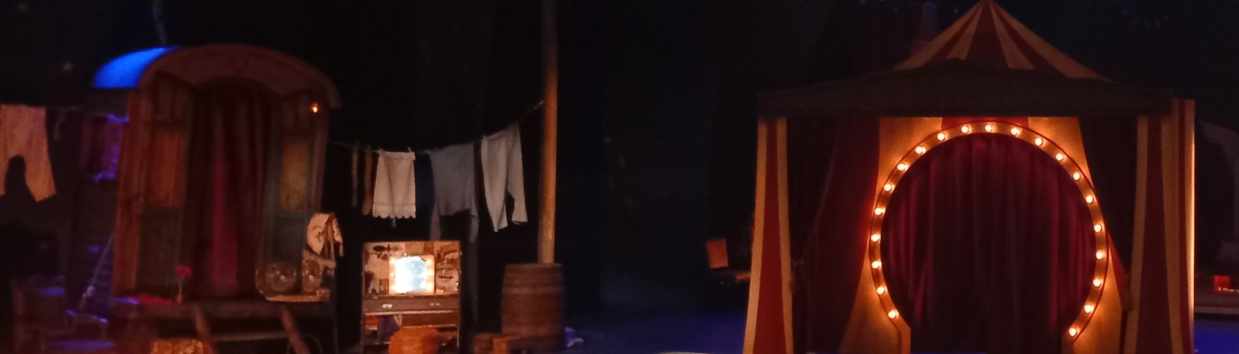 Näyttämökuva, jossa näkyy sirkusvaunu ja sirkuksen areena ja teltta.